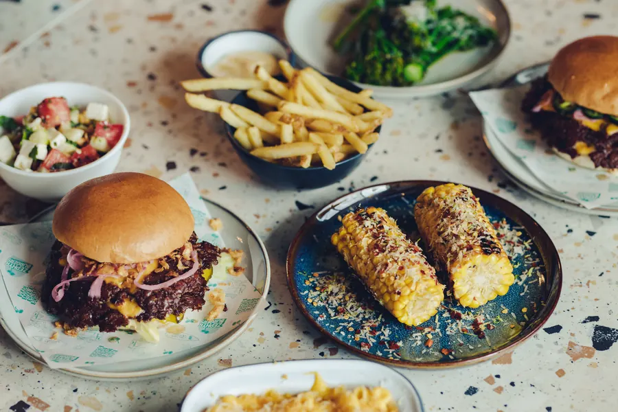 Cheeseburger, corn ribs, fries and slaw spread across a table